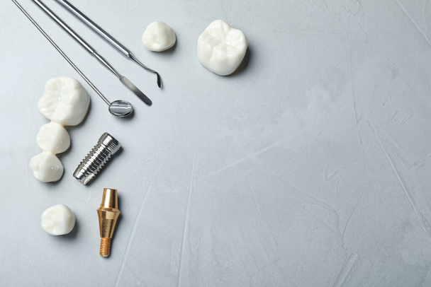 Post, abutment and different crowns of dental implant near medical tools on grey background, flat lay. Space for text - Fotografie, Obrázek