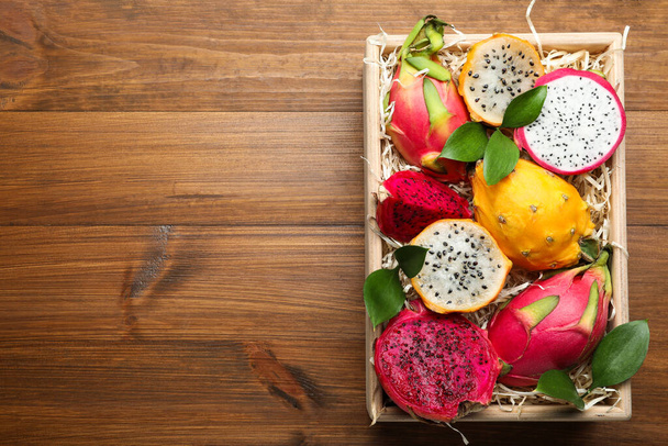 Delicious cut and whole dragon fruits in crate on wooden table, top view. Space for text - Foto, imagen