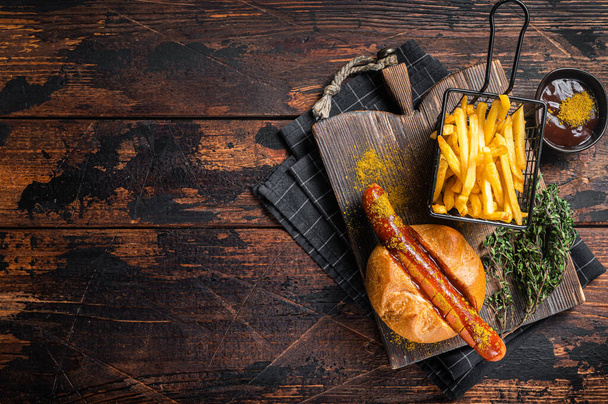 Currywurst Bratwurst sausage in a bun with curry sauce and French fries. Wooden background. Top view. Copy space - 写真・画像