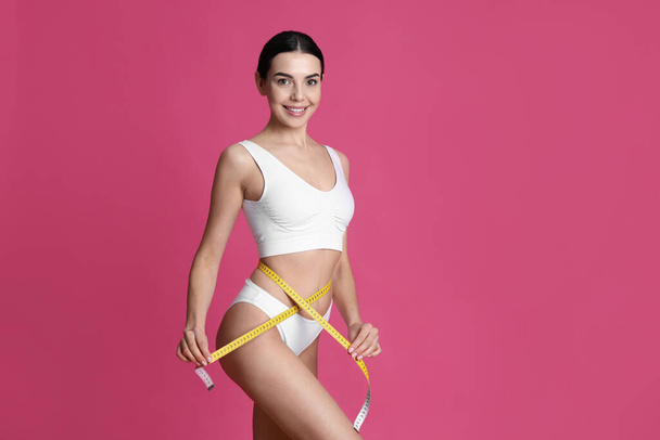 Young woman measuring waist with tape on pink background. Space for text - Foto, immagini