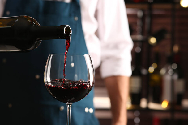 Bartender pouring red wine into glass indoors, closeup. Space for text - Photo, image