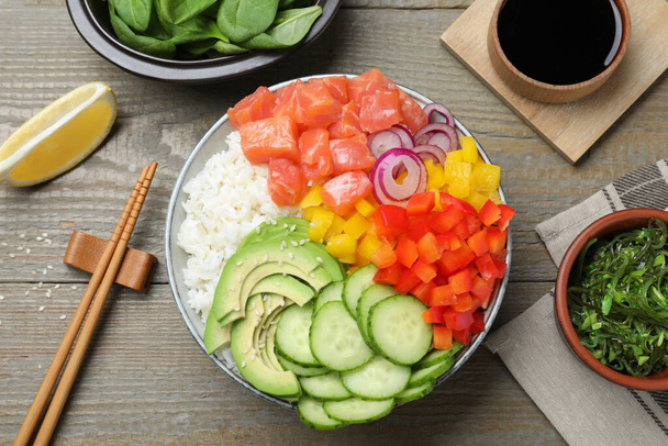 Delicious poke bowl with salmon and vegetables served on wooden table, flat lay - Φωτογραφία, εικόνα
