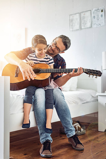 Учу ее различным струнам. Полнометражный снимок красивого взрослого мужчины, который учит свою маленькую дочь играть на гитаре. - Фото, изображение