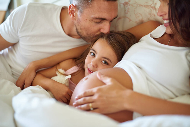 Y pronto habrá cuatro. Foto de una niña feliz acostada en la cama con su padre y su madre embarazada. - Foto, imagen