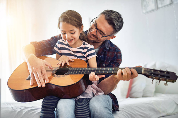 Put your hands like this.... Cropped shot of a handsome mature man teaching his young daughter how to play the guitar. - 写真・画像