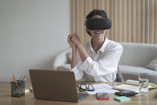 Young overjoyed woman gamer in virtual reality glasses playing simulator game at work - Foto, imagen