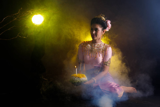 Loykrathong Dress of Thai Traditional Costume or South East Asia gold Dress in Asian Woman with decoration stand express feeling happy smile for Loy Krathong Floating festival over black background - Photo, Image
