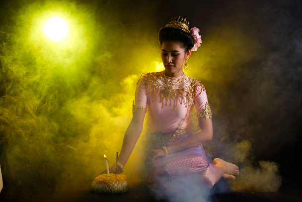 Loykrathong jurk van Thaise Traditionele Kostuum of Zuidoost-Azië goud Jurk in Aziatische vrouw met decoratie staan uitdrukkelijke gevoel blij glimlach voor Loy Krathong Drijvend festival over zwarte achtergrond - Foto, afbeelding