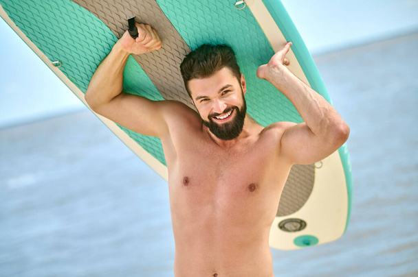 A dark-haired bearded young man carrying kayak - Foto, Bild