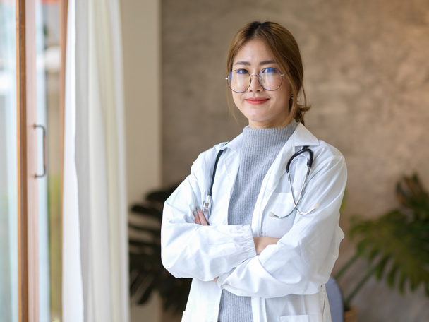 Eine professionelle asiatische Ärztin in weißem Mantel steht mit verschränkten Armen in ihrer Klinik. Arzt, Arzt, Heilpraktiker - Foto, Bild