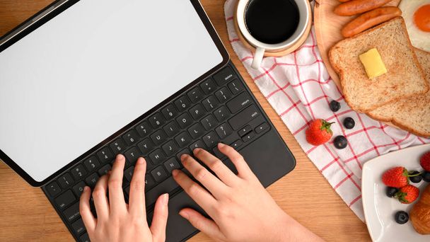 Nainen tai opiskelija työskentelee kannettavan tablet-tietokoneen kanssa näppäimistöllä. Aamiainen pöydällä. - Valokuva, kuva