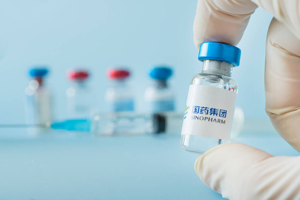 A vaccination syringe and a glass ampoule with a clear liquid on a blue background with the logo of Sinopharm pharmaceutical company. March 15, 2021. Barnaul, Russia. - Foto, Bild
