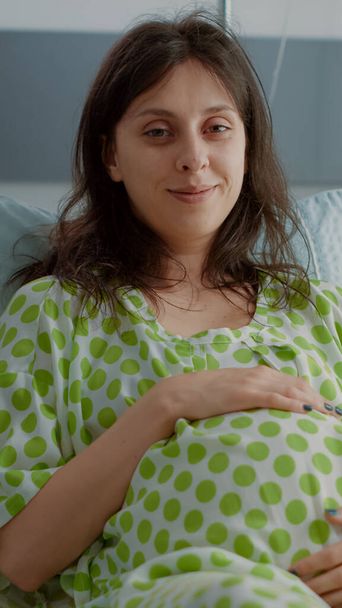 Portrait of adult with pregnancy holding belly in hospital ward - Photo, Image