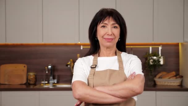 Porträt lächelnde betagte Köchin kreuzt Hände und blickt Kamera in heimische Küche - Filmmaterial, Video
