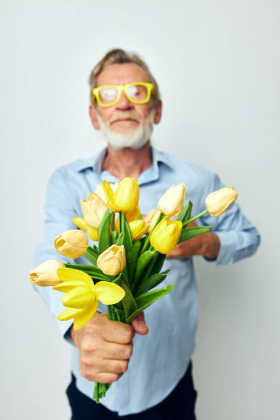 Photo of retired old man in a blue shirt with a bouquet of flowers light background - Foto, Imagem