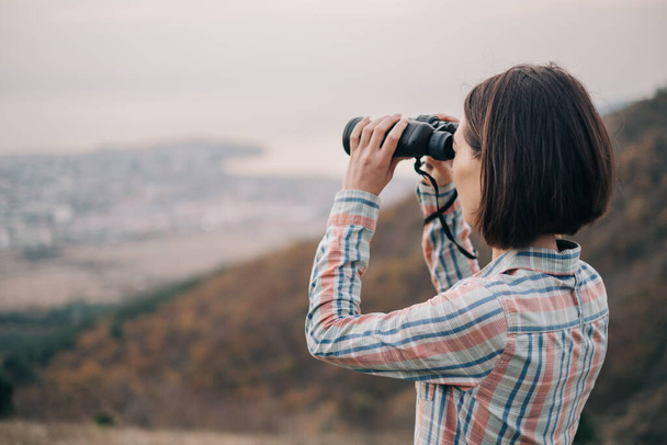 Young woman looks through binoculars and admires the mountain scenery. - Fotoğraf, Görsel