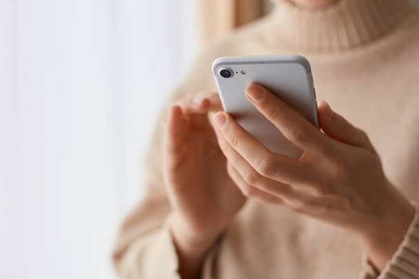 Closeup portrait of anonymous woman wearing beige casual style sweater holding mobile phone in hands, using cell phone for online communication, typing messages. - Foto, immagini