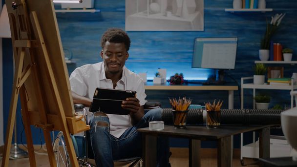 Schwarzer Künstler sitzt mit digitalem Tablet im Rollstuhl - Foto, Bild