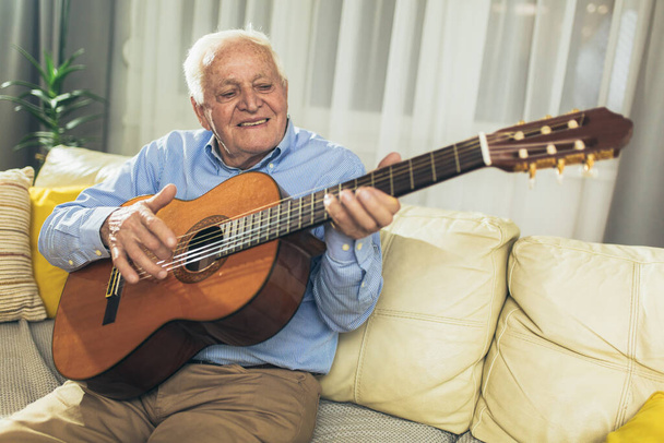Ανώτερος άντρας παίζει κιθάρα στο σαλόνι. - Φωτογραφία, εικόνα