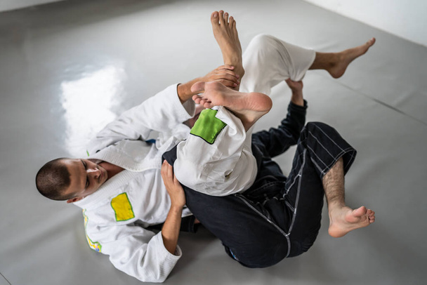 İki Brezilyalı jiu jitsu bjj figörleri dövüş sanatları eğitimi erkek atlet tekniği ya da tatami minderinde siyah beyaz kimono gi üniforması giyerek yedek olmak. - Fotoğraf, Görsel