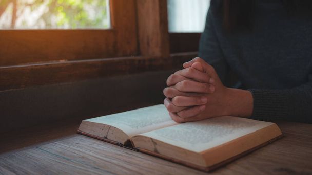 Yakın plan Hıristiyan kadınlar İncil okur. Elleri katlanmış, kutsal bir İncil 'in üzerinde, ahşap bir masanın üzerinde. - Fotoğraf, Görsel