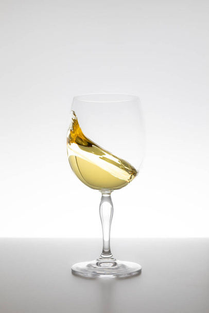 Λευκό κρασί στροβιλίζεται σε ποτήρι σε λευκό φόντο - Φωτογραφία, εικόνα