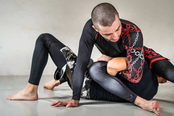 Βραζιλιάνικο jiu jistu bjj no-gi εκπαίδευση πάλης δύο αρρένων αθλητών τεχνική γεώτρησης ή πυγμαχία σε ακαδημία γυμναστικής βραχίονα επίθεση θέση kimura - Φωτογραφία, εικόνα