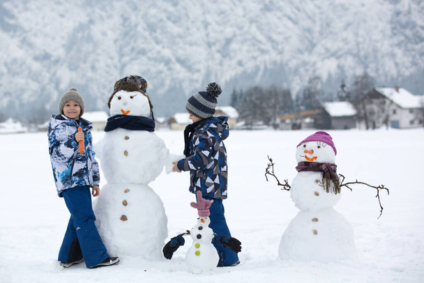 Family with children, building snowman in the park in little village in Austria, beuatiful landscape scenery - Фото, зображення