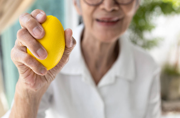 Feszültséglabdát tartó ázsiai idős nő kezei, idős beteg kéz- és csuklógyakorlata, gumilabdával való edzés, izomerő szorítása, ujjgyengeség kezelése, fizikoterápia - Fotó, kép