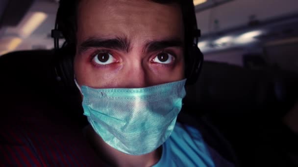 Jovem caucasiano está olhando pela janela durante um voo no avião usando máscara médica - Filmagem, Vídeo