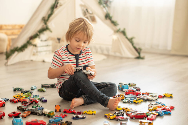 Cute toddler child, blond boy, playing with colofrul cars, different sizes and colors on the floor, smiling - Fotografie, Obrázek