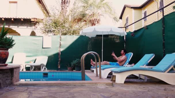 Güneşli yatakta yüzme havuzunun yanında neşeli bir turist akıllı telefondan video görüşmesiyle konuşuyor. - Video, Çekim