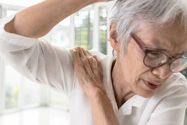 Mujer anciana asiática con dolor en los huesos del hombro, rigidez y dolor al levantar la parte superior del brazo, sufre dificultad para levantar o estirar el brazo de un hombro congelado, inflamación del hombro - Foto, Imagen