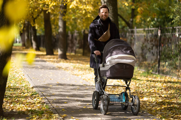 Feliz padre joven con cochecito durante el paseo en la naturaleza
 - Foto, Imagen