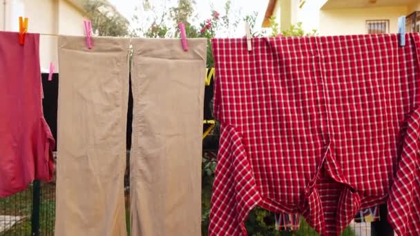 Pantaloni beige e camicia rossa a scacchi sono appesi alla clothesline attaccata da spilli - Filmati, video