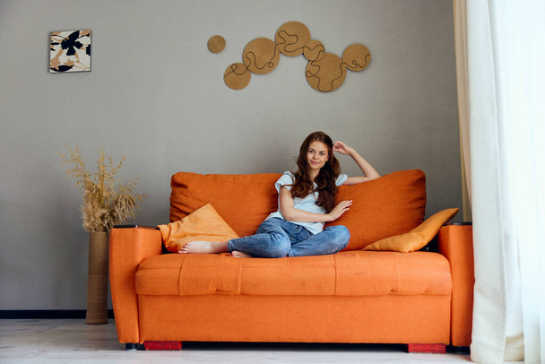 残りの部屋のオレンジのソファの上のきれいな女性は変わらずポーズをとって - 写真・画像