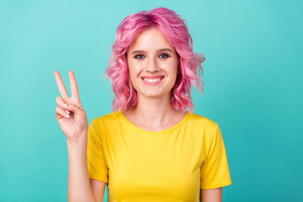 Photo of young funky pink hairdo lady show v-sign wear yellow t-shirt isolated on teal background - Zdjęcie, obraz