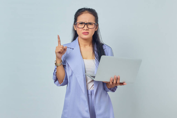 Retrato de mujer asiática joven sorprendida de pie usando el ordenador portátil y apuntando con el dedo al espacio de copia con la boca abierta aislada sobre fondo blanco - Foto, Imagen