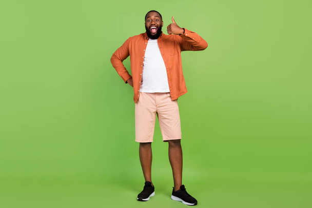 Full body photo of funny millennial brunet guy thumb up wear shirt shorts shoes isolated on green background - Foto, imagen