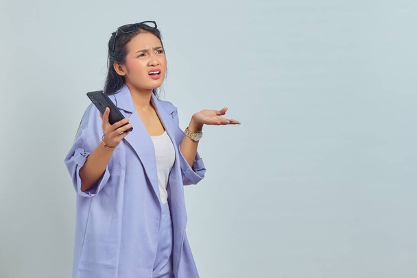 Portrait d'une jeune femme asiatique surprise utilisant un téléphone portable avec bouche ouverte isolée sur fond blanc - Photo, image