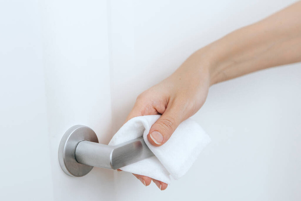 Cleaning door handles with an antiseptic wet wipe and gloves. Sanitize surfaces prevention in hospital and public spaces against corona virus. Woman hand using towel for cleaning home room door link - Valokuva, kuva