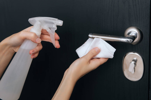 Cleaning black door handles with an antiseptic wet wipe and sanitizer spray. Disinfection in hospital and public spaces against corona virus. Woman hand using towel for cleaning home room door link - Zdjęcie, obraz