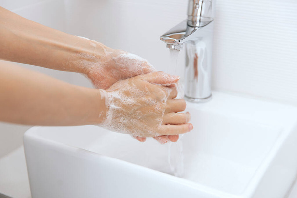 Washing hands under the flowing water tap. Hygiene concept hand detail. Washing hands rubbing with soap for corona virus prevention, hygiene to stop spreading corona virus in or public wash room - Foto, imagen