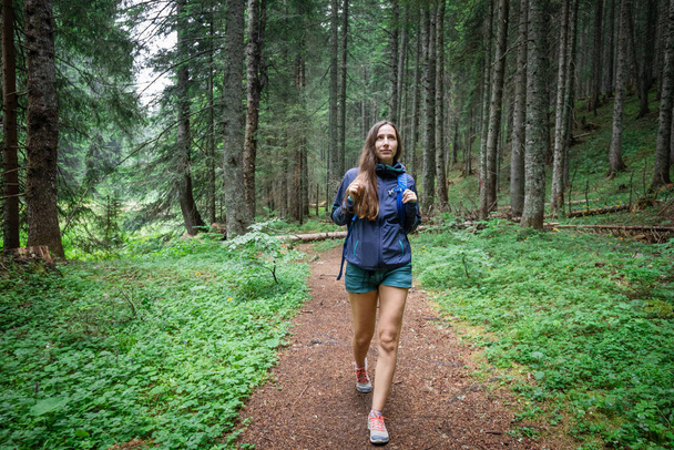 Young smiling woman with backpack walking on footpath in the forest - Valokuva, kuva