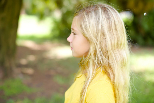 Profile portrait of nice beautiful Caucasian little kid girl wearing yellow T-shirt standing outdoors look empty space toothy smile - Foto, Imagem