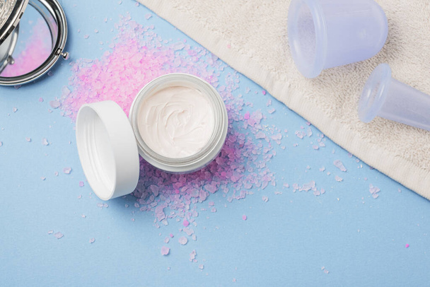 Flatlay with cream, bath rose salt, massage vacuum jars on blu background.Spa and natural skin care concept - Photo, Image