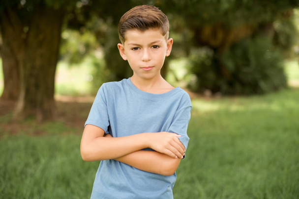 Ernsthaft nachdenkliche schöne kaukasische kleine Junge tragen blaues T-Shirt im Freien stehen fühlen sich wie coole selbstbewusste Unternehmer Crosshands. - Foto, Bild