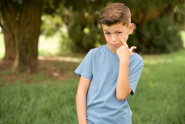 beautiful Caucasian little kid boy wearing blue T-shirt standing Pointing to the eye watching you gesture, suspicious expression. - Foto, Imagen