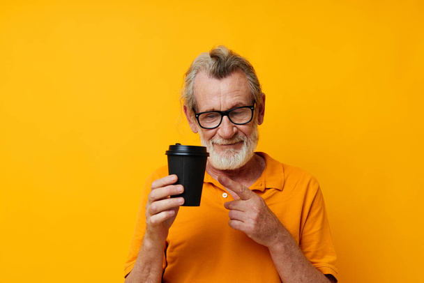 Senior grey-haired man with black disposable cup yellow background - Foto, Bild
