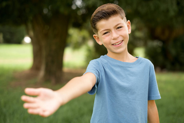 青いTシャツを着た美しい白人の小さな子供は、挨拶と歓迎として握手を提供する笑顔の優しい立っています。成功事業. - 写真・画像